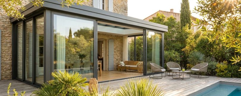 Véranda moderne en aluminium accolée à une maison, baies vitrées, jardin ensoleillé